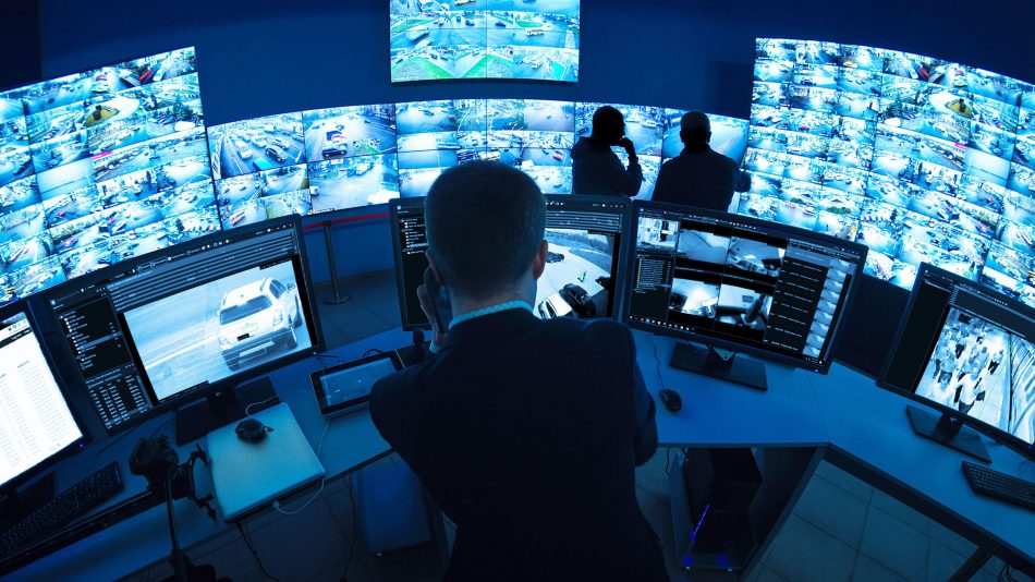 Man in control room with dozens of monitors showing feeds from different cameras, highlighting Senstar's risk mitigation capabilities