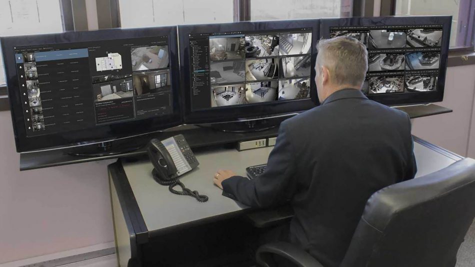 Plataforma de video, seguridad e información Symphony en uso en una sala de control con un hombre sentado frente a múltiples monitores usando una estación de trabajo Senstar